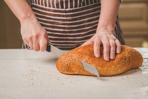 Frau Schneiden Brot auf hölzern Tafel. Backhaus. Brot Produktion. foto