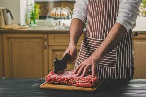 Mann schneidet von frisch Stück von Rindfleisch auf ein hölzern Schneiden Tafel im das Zuhause Küche foto