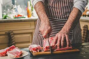 Mann schneidet von frisch Stück von Rindfleisch auf ein hölzern Schneiden Tafel im das Zuhause Küche foto