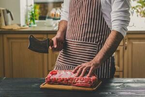 Mann schneidet von frisch Stück von Rindfleisch auf ein hölzern Schneiden Tafel im das Zuhause Küche foto