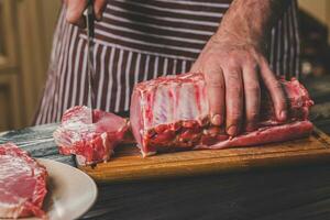 Mann schneidet von frisch Stück von Fleisch auf ein hölzern Schneiden Tafel im das Zuhause Küche foto
