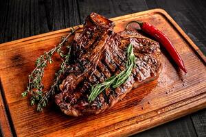 Mittel Selten gegrillt Steak auf rustikal Schneiden Tafel mit Rosmarin und Gewürze , dunkel rustikal hölzern Hintergrund, oben Aussicht foto