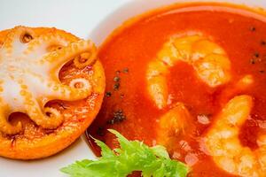 Schüssel von Tomate Suppe mit Garnelen mit ein klein Tintenfisch gebacken auf ein Orange Scheibe. Nahaufnahme, oben Aussicht foto