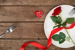 Valentinstag Tag Abendessen Tabelle Rahmen mit rot Band, Rose, Messer und Gabel Ring Über Eiche Hintergrund. foto