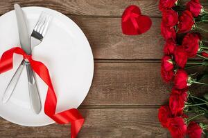 Valentinsgrüße Tag Tabelle Rahmen mit Platte, Gabel, Messer, rot Herz, Band und Rosen. Hintergrund foto