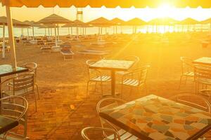 Strand mit Deck Stühle, Sonnenschirm, und Bar während Sonnenaufgang foto