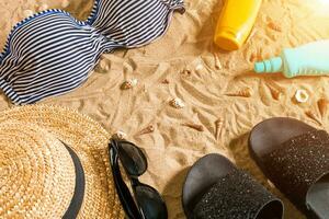 Sommer- Bikini und Zubehör stilvoll Strand Satz, Strand Bikini Sommer- Outfit und Meer Sand wie Hintergrund, oben Sicht, Konzept foto