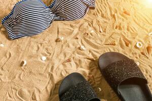 Sommer- Bikini und Zubehör stilvoll Strand Satz, Strand Bikini Sommer- Outfit und Meer Sand wie Hintergrund, oben Sicht, Konzept foto