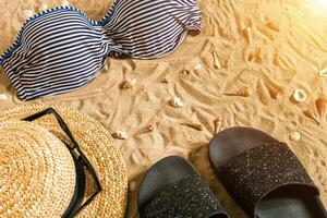Sommer- Bikini und Zubehör stilvoll Strand Satz, Strand Bikini Sommer- Outfit und Meer Sand wie Hintergrund, oben Sicht, Konzept foto