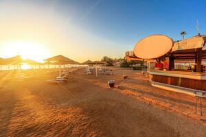 Strand mit Deck Stühle, Sonnenschirm, und Bar während Sonnenaufgang foto