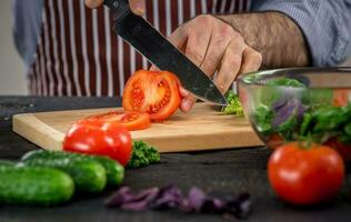 männlich Hände Schneiden Gemüse zum Salat foto