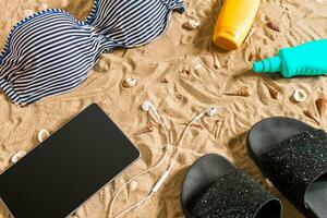 Sommer- Bikini und Zubehör stilvoll Strand Satz, Strand Bikini Sommer- Outfit und Meer Sand wie Hintergrund, oben Sicht, Konzept foto