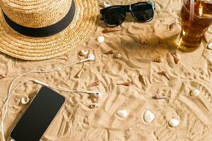 Sommer- Strandkleidung, Sonnenbrille, Hut, kalt trinken im ein Glas und Muscheln auf Sand Strand. foto