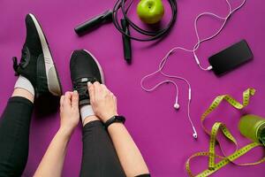 jung Frau Schnürsenkel Turnschuhe, vorbereiten zum Ausbildung. Flasche von Wasser, Yoga Matte, Telefon, Kopfhörer auf lila Hintergrund eben legen oben Sicht. foto