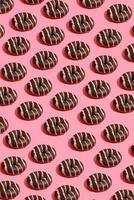 Essen Design mit lecker Schokolade glasiert Krapfen mit Weiß Streifen auf Koralle Rosa Pastell- Hintergrund oben Aussicht Muster foto