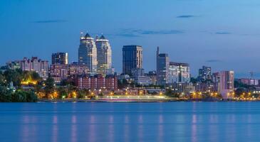 Panorama- Aussicht von das Türme, Wolkenkratzer, Promenade im das Abend, das Beleuchtung sind reflektiert auf das Dnjepr Fluss, Ukraine. dnipro Stadt, Dnipropetrowsk. foto
