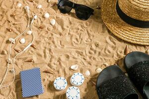 Strandpoker. Chips und Karten auf das Sand. um das Muscheln, Sonnenbrille und Flip Flops. oben Aussicht foto