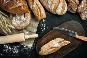 frisch brot, hölzern Tafel und Schneiden Messer auf schwarz Tabelle foto