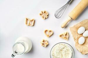 Objekte und Zutaten zum Backen, Plastik Formen zum Kekse auf ein Weiß Hintergrund. Mehl, Eier, rollen Stift, Schneebesen, Milch, Butter, Creme. oben Sicht, Raum zum Text foto