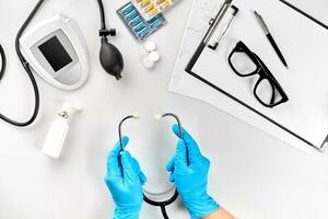 Arbeitsplatz von ein Arzt Operation, Hand im Handschuh halten Stethoskop, Zwischenablage auf Schreibtisch Hintergrund. oben Aussicht foto
