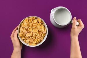 Essen und Menschen Konzept Hände von Frau Essen Getreide Mais Flocken zum Frühstück und Gießen Milch foto