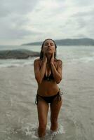 Herrlich Brünette Frau mit perfekt Zahl posieren auf tropisch Strand. tragen stilvoll schwarz Bademode. foto
