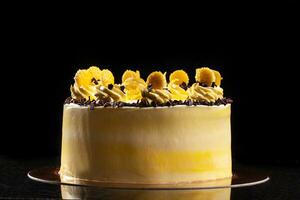 runden Gelb Geburtstag Kuchen. dekorativ Sahne Dekorationen auf das Kuchen. schwarz Hintergrund. foto