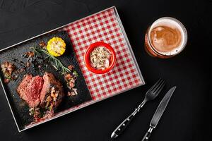 geschnitten Mittel Selten gegrillt Rindfleisch Steak Rippenstück mit Mais, Rosmarin, Zwiebel und Pilz Soße auf ein Metall Tablett auf ein schwarz Hintergrund foto