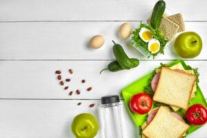 Mittagessen. Sandwich und frisch Gemüse, Flasche von Wasser, Nüsse und Früchte auf Weiß hölzern Hintergrund. gesund Essen Konzept. oben Aussicht mit Kopieren Raum foto