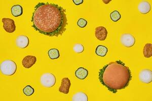 die meisten Beliebt schnell Essen Mahlzeit. Hähnchen Nuggets, Burger mit frisch Gurke und Zwiebeln auf Gelb Hintergrund oben Aussicht foto