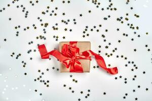Geschenk mit rot Bogen auf Weiß Hintergrund mit metallisch Star geformt Konfetti. eben legen Stil foto