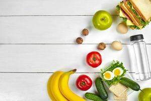 Mittagessen. Sandwich und frisch Gemüse, Flasche von Wasser, Nüsse und Früchte auf Weiß hölzern Hintergrund. gesund Essen Konzept. oben Aussicht mit Kopieren Raum foto