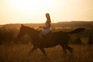 Mädchen auf einem Pferd bei Sonnenuntergang foto
