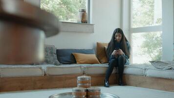 Mädchen sitzt in der Ecke des Wohnzimmers und tippt auf dem Smartphone foto