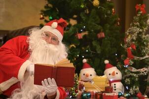 Santa claus lesen rot Buch im Zimmer dekoriert zum Weihnachten Feier beim Nacht foto