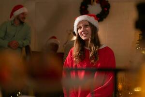 Porträt von Teenager Mädchen im Santa Hut Sitzung auf Stuhl im Vorderseite von Weihnachten Baum, fröhlich Weihnachten und glücklich Ferien foto