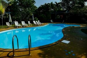 ein Schwimmen Schwimmbad im ein Hinterhof mit Rasen Stühle und Regenschirme foto