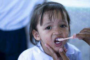 ein Pflege Mutter sanft Bürsten ihr wenig Tochter Zähne zum gut Dental Gesundheit. foto