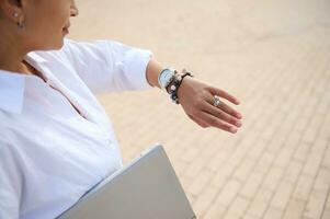 Nahansicht von das Hand von ein Geschäftsfrau , weiblich Unternehmer mit Laptop, Überprüfung Zeit auf ihr Handgelenk Uhr foto