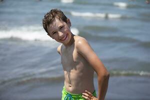 glücklich Junge ist ruhen durch das Meer, suchen beim das Kamera. Kind auf Ferien beim das Strand. foto