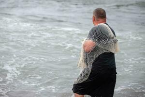 ein Fischer mit ein Angeln Netz tritt ein das Meer. foto