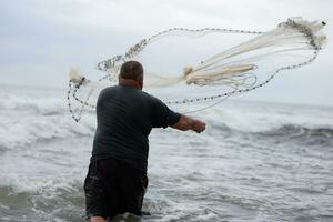ein Fischer wirft ein Angeln Netz in das Meer. foto