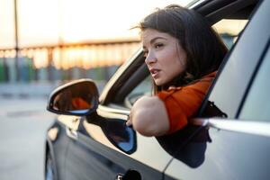 jung Frau spähen aus von Auto Fenster. Frau mit im das Wind lehnt sich aus von das Auto Fenster und suchen Gerade mit Kopieren Raum. foto