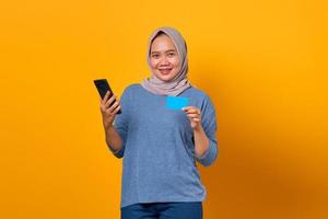 fröhliche asiatische frau, die handy hält und kreditkarte zeigt foto
