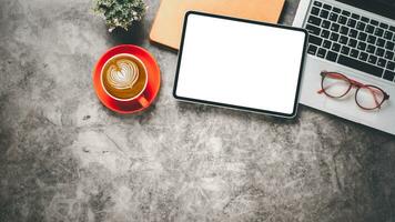 Büro Schreibtisch Arbeitsplatz mit leer Bildschirm Tablette, Laptop, Notizbuch, Brille und Tasse von Kaffee, oben Aussicht eben legen mit Kopieren Raum. foto