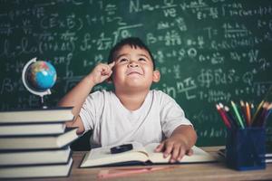 nachdenklicher kleiner Junge mit Buch im Klassenzimmer foto
