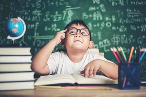 nachdenklicher kleiner Junge mit Buch im Klassenzimmer foto