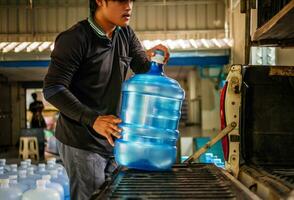 Arbeitskräfte Aufzug Trinken Wasser klar und sauber im Blau Plastik Gallone in das zurück von ein Transport LKW gereinigt Trinken Wasser Innerhalb das Produktion Linie zu bereiten zum Ausverkauf.klein Geschäft foto