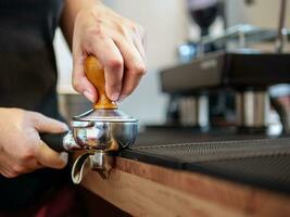 Hand von ein Barista halten ein Siebträger und ein Kaffee manipulieren Herstellung ein Espresso Kaffee. Barista drückt Boden Kaffee mit ein manipulieren im ein Kaffee Geschäft foto