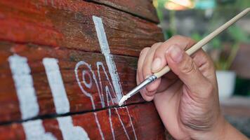 Nahansicht von Hände von jung Frau Maler Erstellen Kunst verwenden ein Pinsel zu zeichnen Weiß Beschriftung Designs auf ein hölzern Kaffee Geschäft sign.outdoor Aktivitäten, Menschen tun Aktivitäten. foto